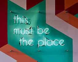Neon sign on painted wall reading 'This must be the place'