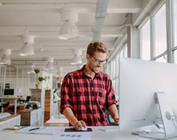 Standing Man in Red Checkered Shirt Working On A Laptop
