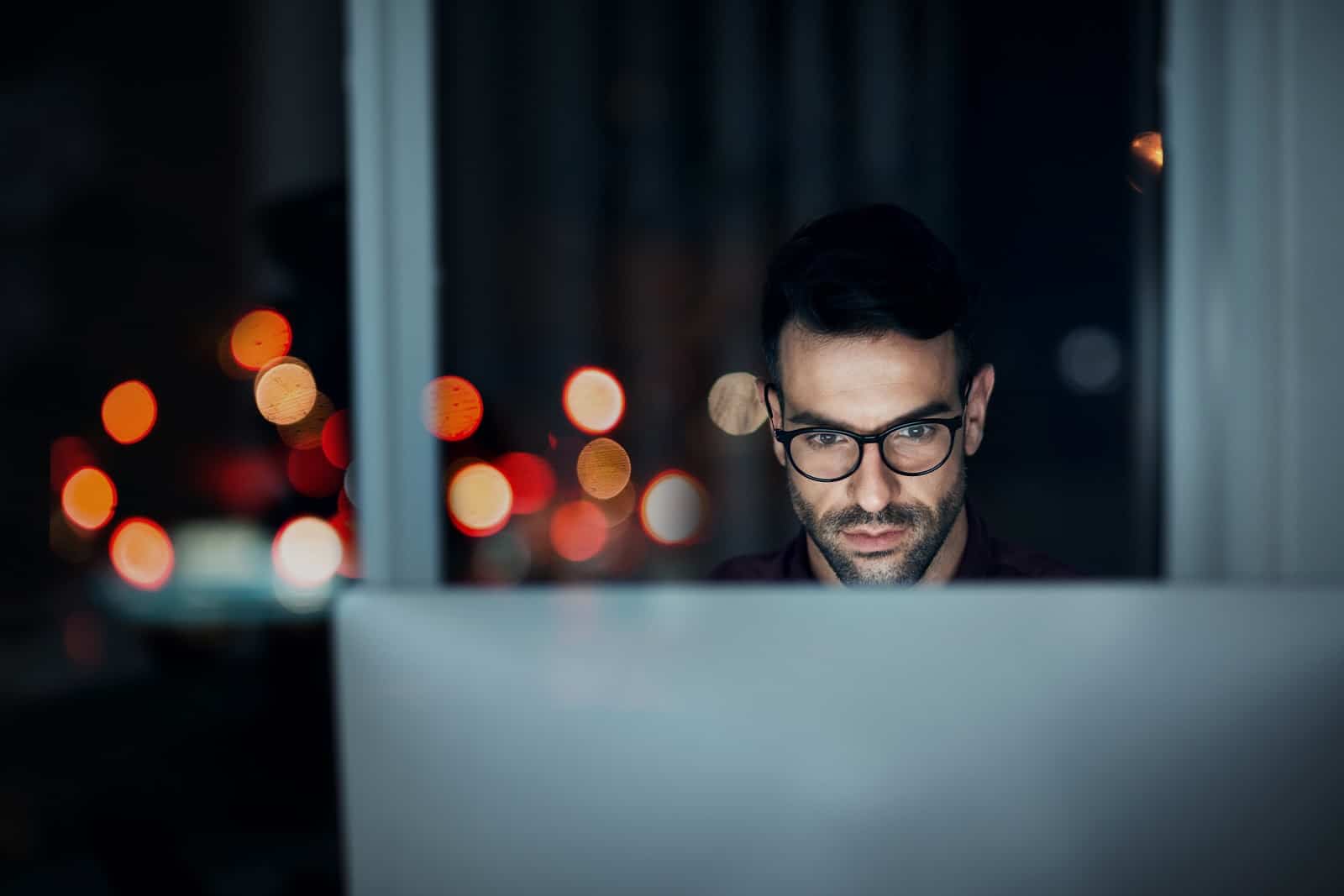 Man sitting at his office desk at night with computer screen in front of him