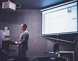 Man Speaking at The Conference Room With Projector on The Background
