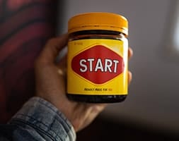 Person holding a jar of Vegemite with the word start printed on the label