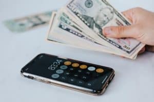 A Hand Holding Dollars and A Calculator on The Table