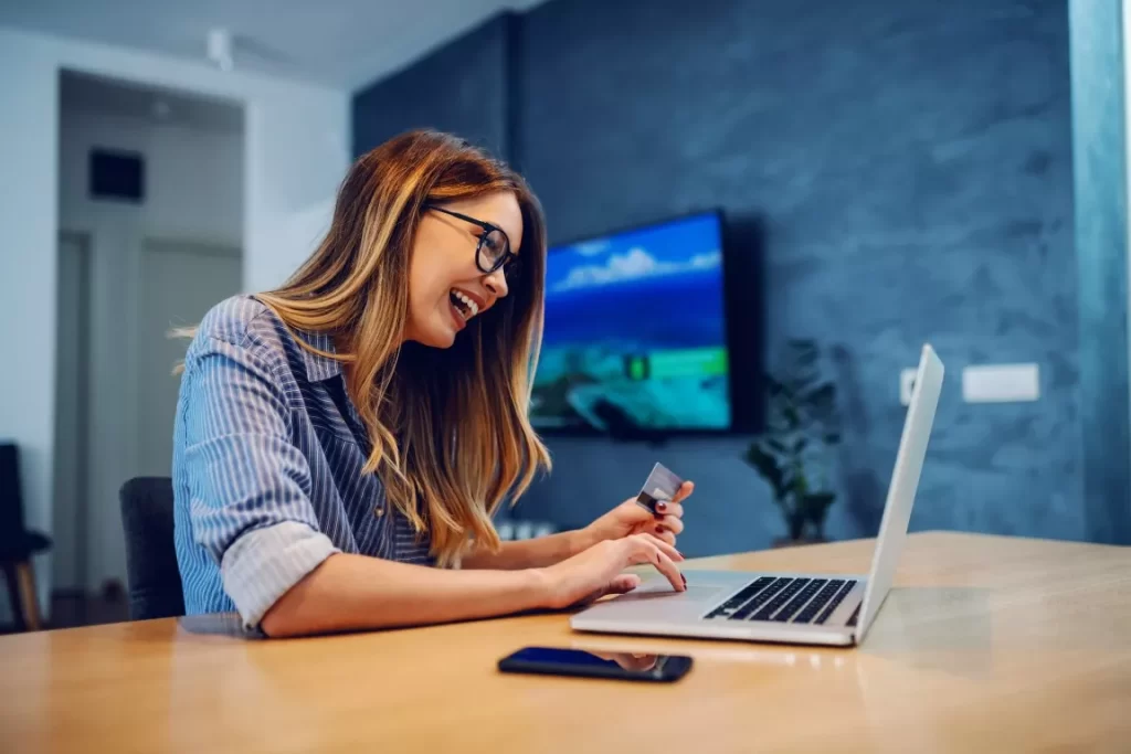 Happy Woman With A Card on Hand Looking at The Laptop