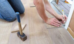 A person beside a mallet measuring the floor with pencil.