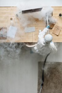 A person wearing PPE fumigating a computer desk