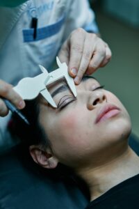 A plastic surgeon measuring a female patient’s eyelid with a medical instrument